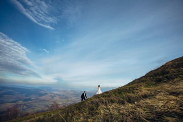 Groom walks behind bride to the top of autumn hill