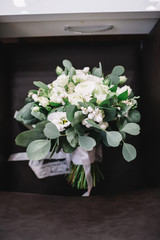 White wedding bouquet with green leaves lies on the chair
