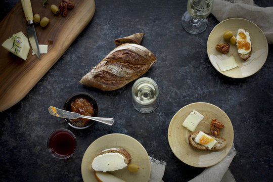 Fromage Fort Cheese Spread served with French bread, spicy pecans, quince jam, Manchego, olives, pears and an assortment of wine. Photographed on black/grey/brown background.