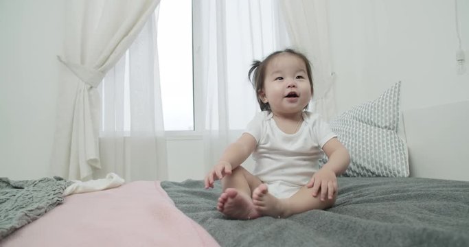 slow motion, little Asian girl 1 year baby ,having fun on the bed in the room , emotionally expresses joy