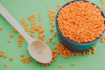 Red lentil in bowl and wooden spoon on green background