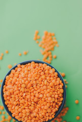 Red lentil in bowl and wooden spoon on green background