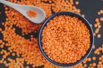 Red lentil in bowl with spoon on black background