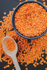 Red lentil in bowl with spoon on black background