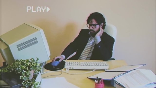 Fake VHS tape: a male employee at work in the office is bored and unproductive. The boss scolds him, he resumes working.
