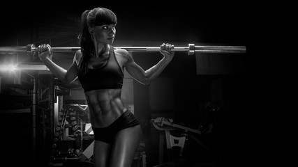 Black and white photo of fit young woman in great shape lifting barbells looking focused, working...