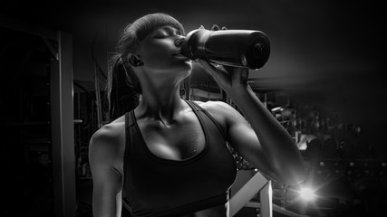 Black and white photo of fitness woman drinking water from bottle Muscular young female at gym taking a break from workout
