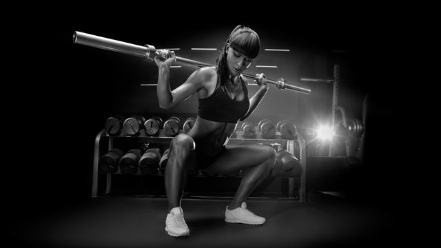 Black and white image of fit young woman in great shape lifting barbells looking down