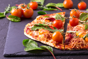 Homemade pizza with bacon, tomatoes, spinach, arugula and cheese