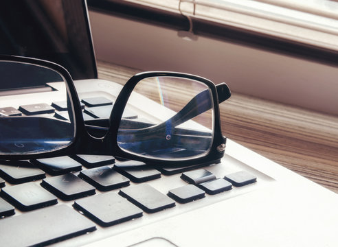Glasses and the keypad of the computer at a window from blinds.