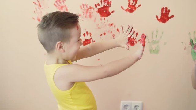 Young mother with her little boy are lmixing colors at their hands yo leave beautiful handprints on the wall. Mother and child concept. Slowmotion.