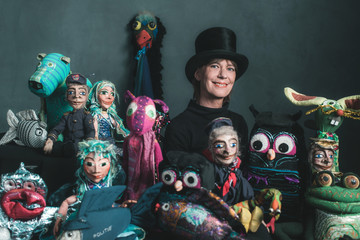 Smiling puppeteer standing between handmade puppets.