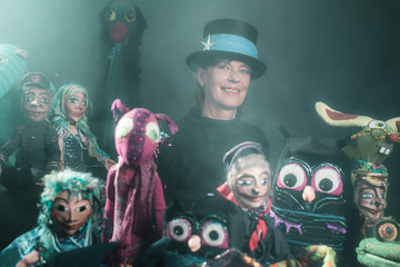 Mystical puppeteer standing between handmade puppets.
