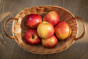 Fresh red apples in basket over wooden background