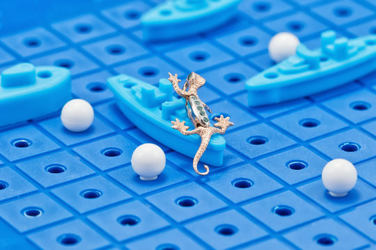 Pendant in the form of a gold Salamander attacks a toy warships on Board game