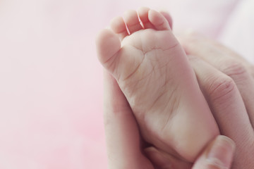 Closeup of mother hands holding cute tiny baby feet, showing baby foot. Selective focus. Toned.