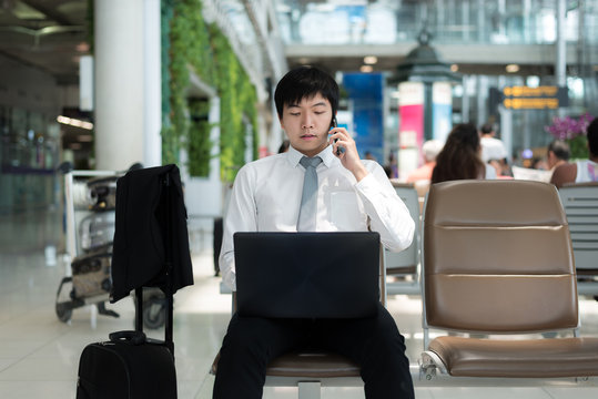 Asian businessman using smartphone and laptop while waiting for his flight in terminal at airport.
