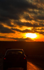 Fototapeta na wymiar Highway road and car in front of orange sunset sky at winter