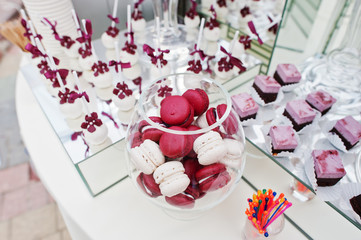 Red and white macarons at wedding catering table with different sweets.