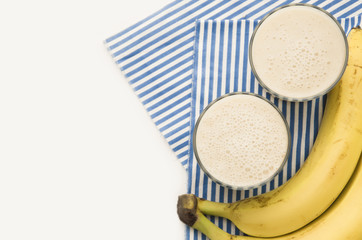 Useful smoothies with a banana and oatmeal on a white background, in glass bowls on a striped tablecloth. View from above. Picture with space for text or logo