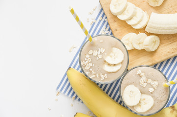 Useful smoothies with a banana and oatmeal on a white background, in glass bowls on a striped tablecloth. View from above. Picture with space for text or logo