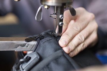 Tailor man sews up a bag in a workshop