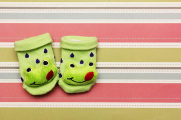Cute baby socks with frog figure on colorful background.