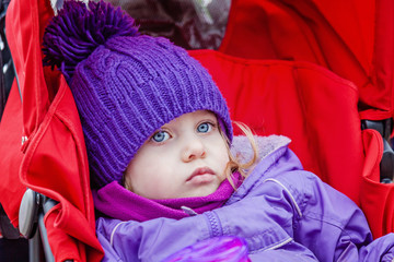 Sad or bored little girl sitting in stroller.  Selective focus on child face.