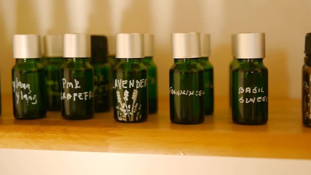 Signed glass bottles of essential oil for aromatherapy are on spa salon wooden shelf.  Pan shot