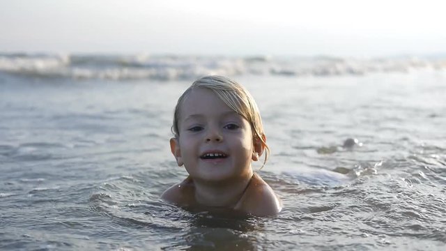 A little child playing in sea waves,  cute boy splashing in water on the sunset in slow motion x2 with backlight sun