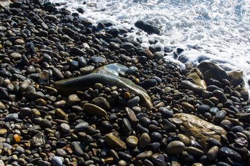 sea pebble beach with multicoloured stones, waves with foam