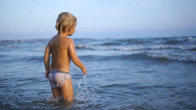 A happy chid jumping through the sea waves in the surf on a summer vacation in slow motion x2