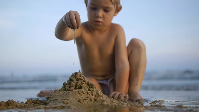 Potrait of little child making sand castle on beach on sea background in sunset in slow motion x2