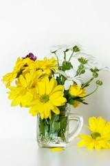Beautiful bouquet of yellow and white chrysanthemum in little glass cup with a handle, used as a vase, on white background. Spring concept. 