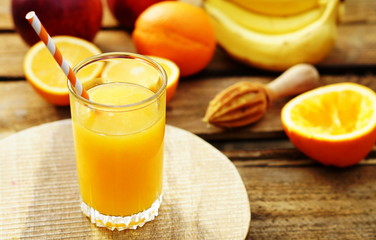 Freshly squeezed orange juice in glass with ice cubes and juicer on wooden board