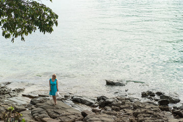 Young woman in blue dress staying on the rocky beach