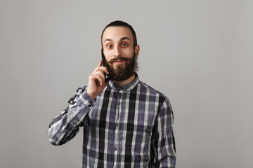 Bearded handsome man is talking by phone in blue squared shirt on grey background