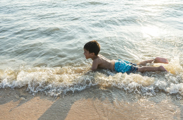 happy asian boy playing in the water waves at sea ocean