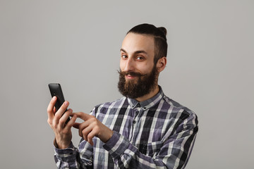 Bearded handsome man is chatting by phone in blue squared shirt on grey background