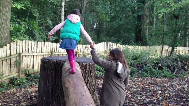 Young girl holding mummies had as she balances on a log in outdoor play area