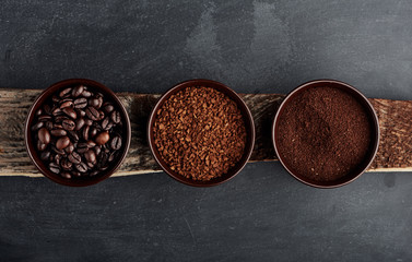 Three kinds of coffee: beans, milled, instant in cups on wooden plank. 
