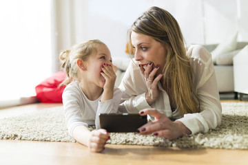 Beautiful mother and daughter playing with mobile phone at home.