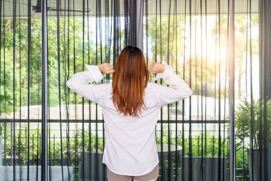 Woman stretching her arms while standing and looking sunrise through the window in the morning.