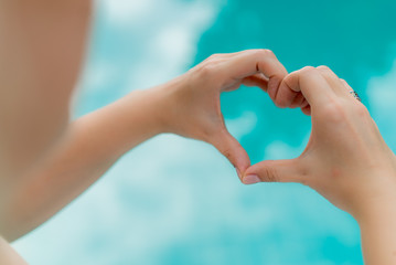 Woman shows heart by hands, pool on background