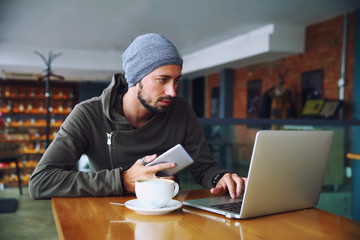 Young handsome hipster man with beard is using computer in cafeteria
