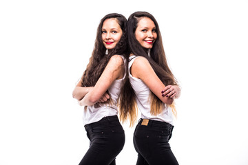 Portrait of a young serious sisters twins standing back to back with arms folded isolated