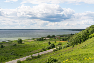 Fototapeta na wymiar Lake, empty road, hill and plain. Stormy clouds and horizon on background. Romantic deserted landscape of middle Russia.