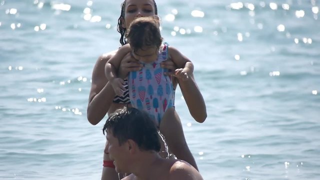 Young girl putting on her shoulders cute little child. Happy family enjoying sea waves on summer vacation. Slow motion 50Fps.