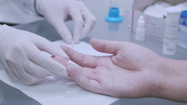 Finger blood test. Doctor doing blood analysis. Closeup of doctor hands in gloves doing blood testing. Close up of doctor hands using lancelet for blood diagnostic. Doctor doing medical analysis