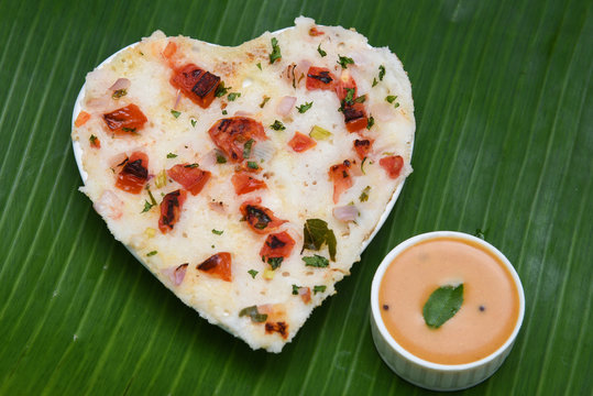 South Indian breakfast Oothappam / Dosa heart shape cooked using rice lentil and vegetables served with coconut chutney and sambhar isolated on coir. popular dish in Kerala and Tamil Nadu India.